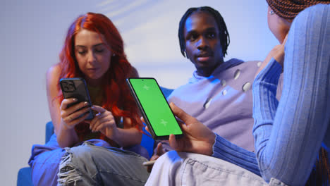 Close-Up-Of-Woman-With-Green-Screen-Mobile-Phone-Sitting-With-Gen-Z-Friends-Talking-And-Sharing-Posts-2